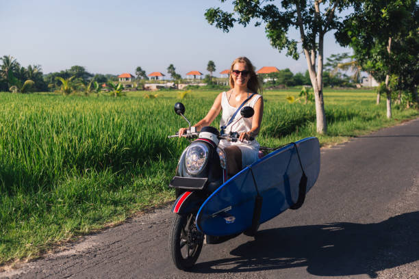 istock young smiling woman riding scooter with surfing board 947819606