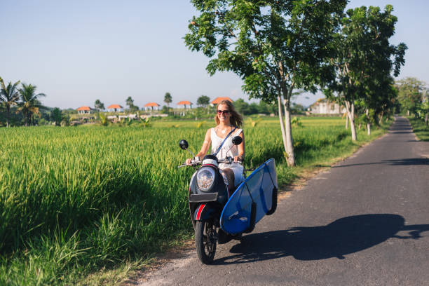 istock young smiling woman riding scooter with surfing board 947820234