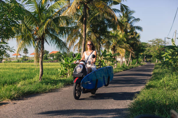 istock young woman riding scooter with surfing board 947821102
