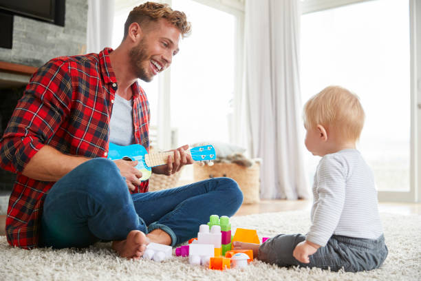 istock Father playing ukulele with young son at home, close up 947844566