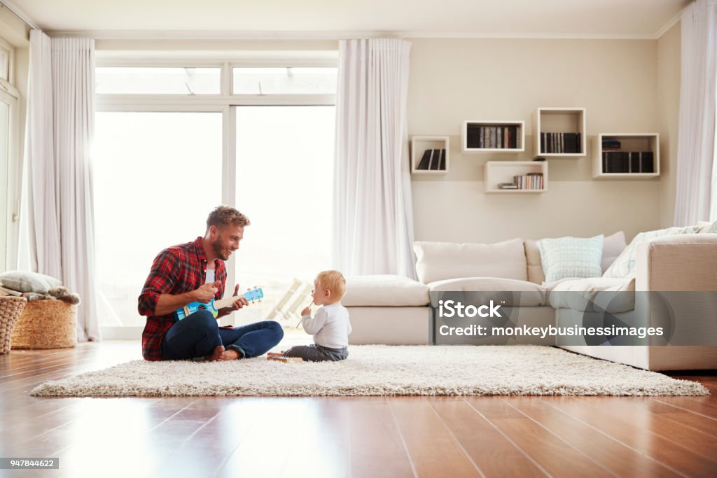 Father playing ukulele with young son in their sitting room Family Stock Photo