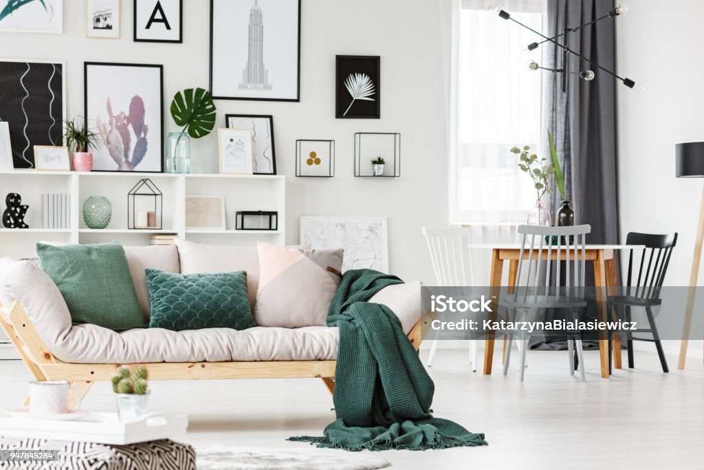 Sofa with cushions and blanket White sofa with cushions and green blanket standing next to a dining table in living room interior Sofa Stock Photo