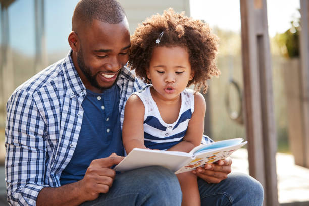 istock Young black father and daughter reading book outside 947848650