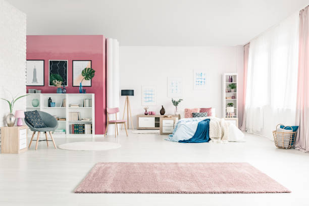 Open space bedroom interior Open space bedroom interior with big rug, cozy bed, pink and white walls, chairs, posters, basket, pink drapes and bookcases round wooden chair stock pictures, royalty-free photos & images