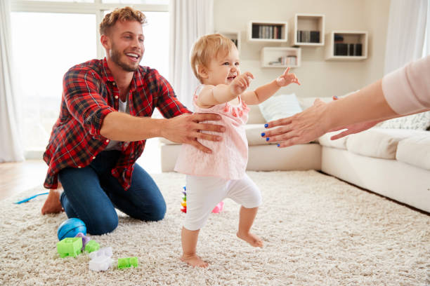 малыш девушка ходить от папы к маме руки в гостиной - young family family with one child walking learning стоковые фото и изображения