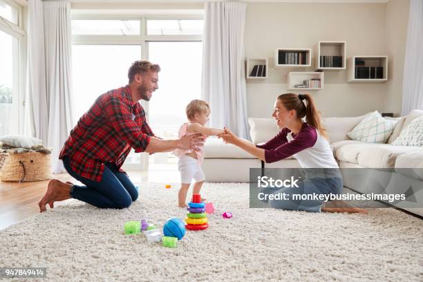 Toddler Girl Walking From Dad To Mum In Sitting Room Stock Photo - Download Image Now
