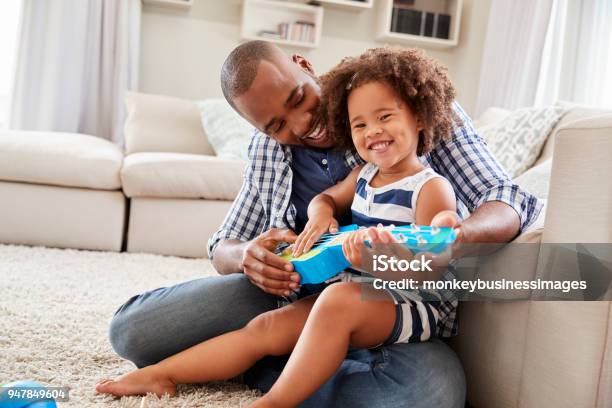 Toddler Daughter Sits On Dadõs Knee Playing Ukulele At Home Stock Photo - Download Image Now