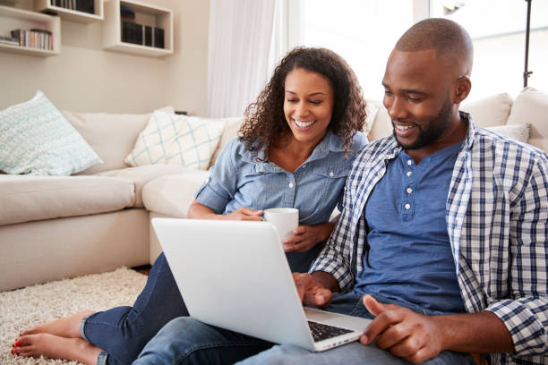 istock Young black couple using laptop sitting on the floor at home 947852650