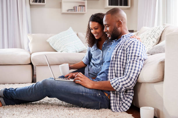 istock Young black couple using laptop sitting on the floor at home 947852724