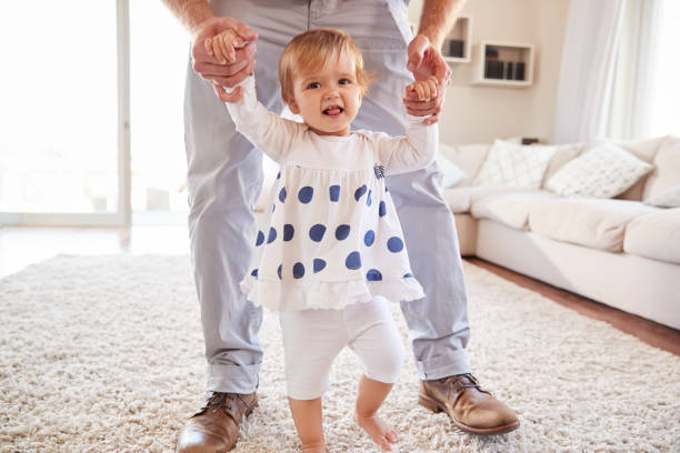 istock Father helping daughter learn to walk in the sitting room 947853324