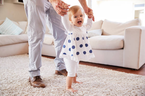 istock Father helping daughter learn to walk in the sitting room 947853434