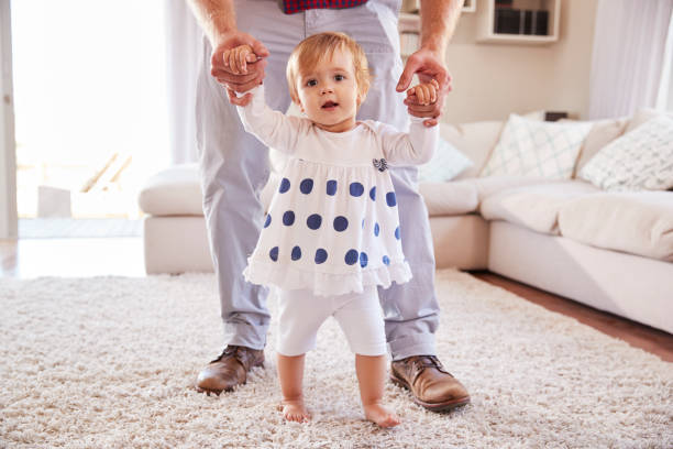 istock Father helping daughter learn to walk in the sitting room 947853462