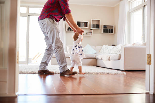 Father helping daughter learn to walk at home, side view Father helping daughter learn to walk at home, side view first steps stock pictures, royalty-free photos & images