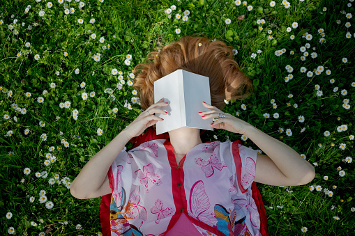Woman's holding a book in front of her face, lying on grass