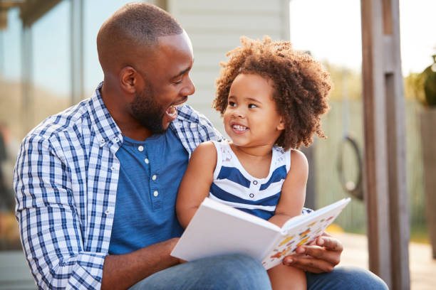 istock Young black father and daughter reading book outside 947854076