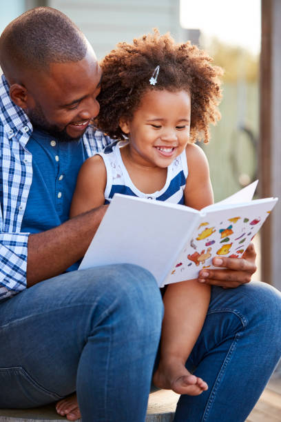 istock Young black father and daughter reading book outside 947854114
