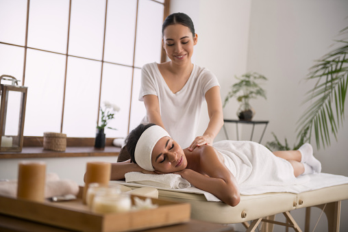 Skillful masseuse. Cheerful Asian woman smiling while doing massage for her client
