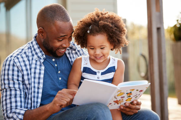 jeune noire père et livre de lecture fille à l’extérieur - family reading african descent book photos et images de collection