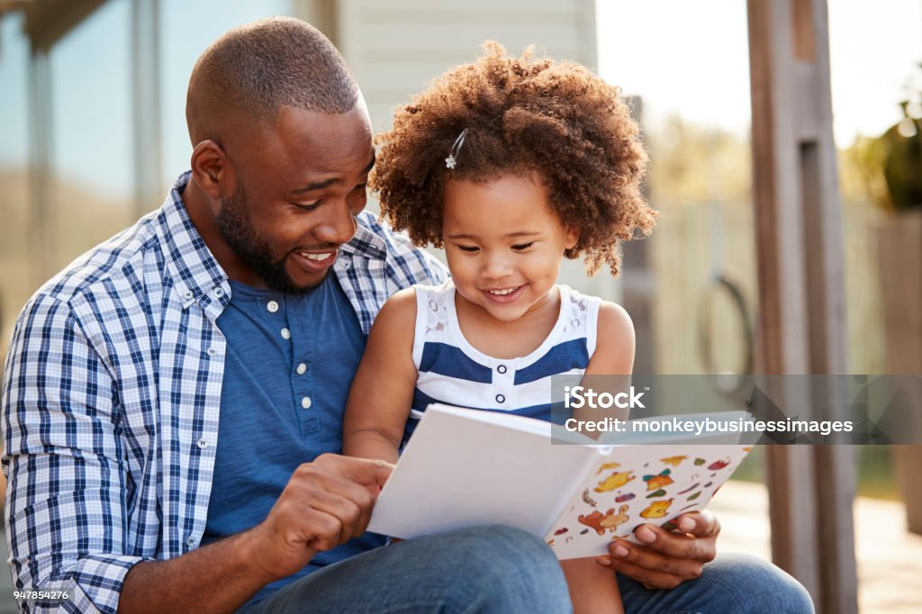 Young black father and daughter reading book outside Reading Stock Photo
