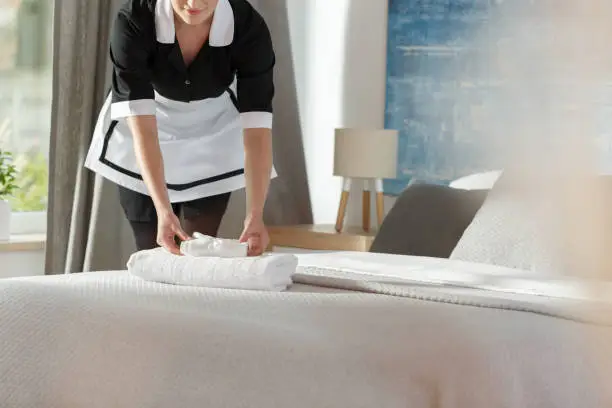Young maid laying fresh towels on a bed in hotel room