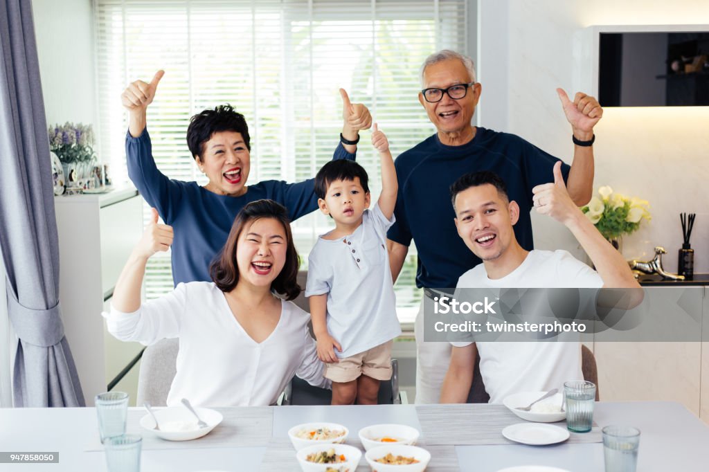 Asiatische Großfamilie aus drei Generationen, die eine Mahlzeit zusammen und zeigt Daumen sich zu Hause mit Glück - Lizenzfrei Familie Stock-Foto