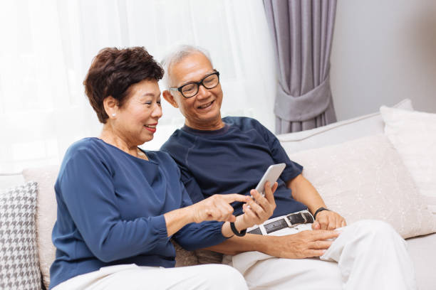 hochrangige asiatische paar großeltern mit einem smartphone zusammen zu hause auf sofa - women telephone senior adult on the phone stock-fotos und bilder