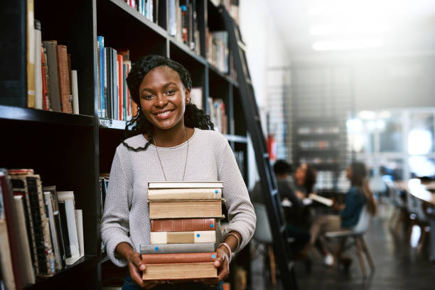 You don't have to look far to find the answers Portrait of a happy young woman carrying books in a library at college librarian stock pictures, royalty-free photos & images