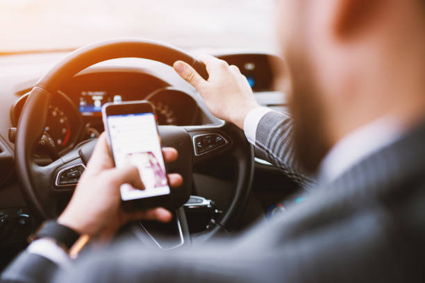istock Rare view of a suited man checking a text while driving a car on a beautiful sunny day. 947913942