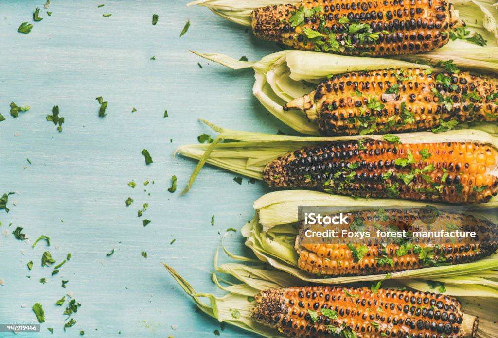 Grilled sweet corn with cilantro over blue background, copy space Summer vegan dinner or snack. Flat-lay of grilled sweet corn with smoked sea salt and cilantro over blue background, top view, copy space. Vegetarian, healthy, clean eating, alkaline diet concept Corn Stock Photo