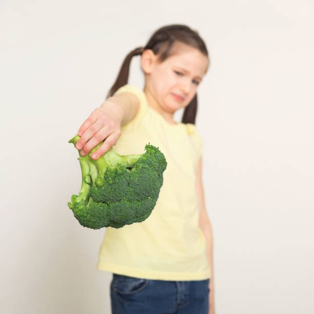 istock Disgusted little girl with broccoli over white background 947925150