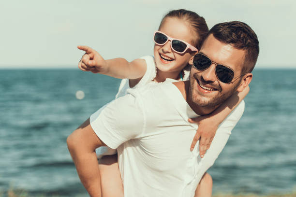 happy little daughter in sunglasses sits on fathers back. - tourist resort fotos imagens e fotografias de stock