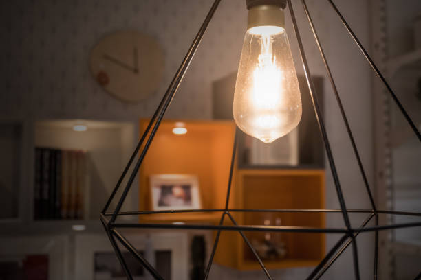 istock A glowing light bulb in modern lamp with blurred decoration shelf background 947951720