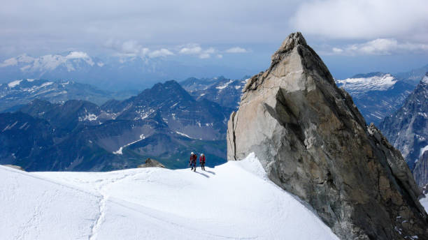 istock mountain guide and client walk along a narrow snow ridge with a giant rock needle and a fantastic view behind them 947952282