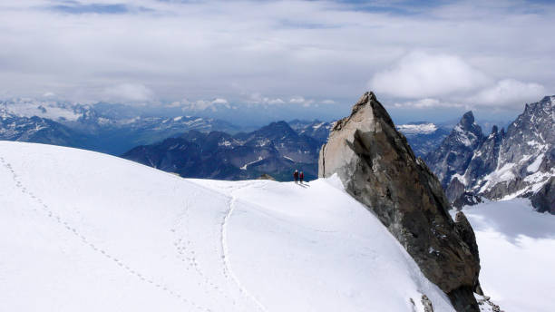 istock mountain guide and client walk along a narrow snow ridge with a giant rock needle and a fantastic view behind them 947952600