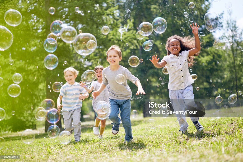 Little Kids Having Fun Outdoors Multi-ethnic group of little friends with toothy smiles on their faces enjoying warm sunny day while participating in soap bubbles show Child Stock Photo