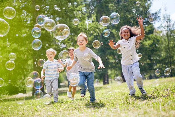 Little Kids Having Fun Outdoors Multi-ethnic group of little friends with toothy smiles on their faces enjoying warm sunny day while participating in soap bubbles show catching photos stock pictures, royalty-free photos & images
