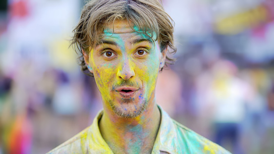 Surprised young man covered in colorful dyes enjoying atmosphere at festival, stock footage