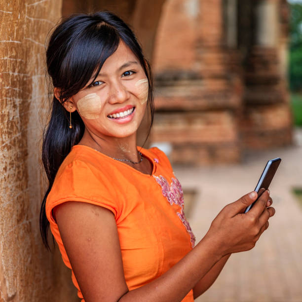 Young Burmese girl using a mobile phone in Bagan, Myanmar Young Burmese girl with thanaka face paint using a smart phone in the ancient temple of Bagan, Myanmar (Burma) bagan archaeological zone stock pictures, royalty-free photos & images