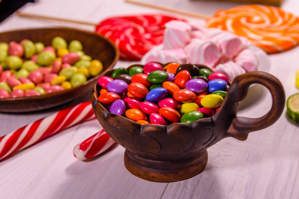 istock Ceramic bowl with colored candies, lollipops and marshmallows on a wooden table 947972338