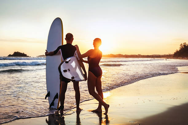 istock Couple surfers stay on sunset ocean beach 947975036