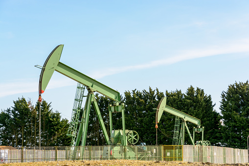Two active pumpjacks pumping oil out of a well located in the center of France under a blue sky.