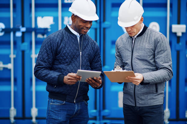 istock Smiling engineers standing in a shipping yard tracking inventory 947982500