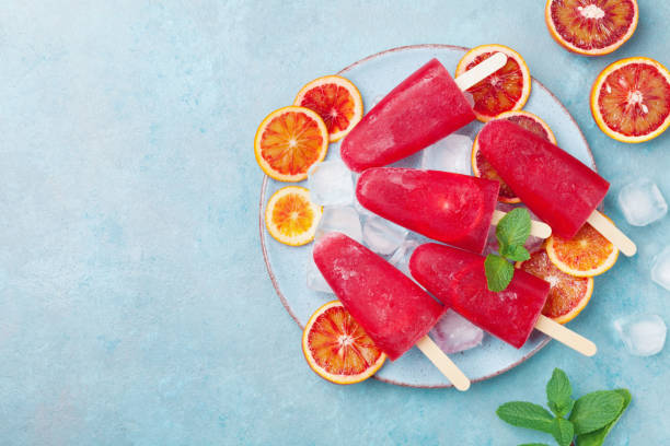 istock Red citrus ice cream or popsicles decorated mint leaves and orange slices on blue table from above. Frozen fruit juice. 947984182