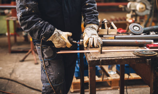 istock Fabric worker in protective uniform cutting metal pipe on the work table with an electric grinder in the industrial workshop. 947989830
