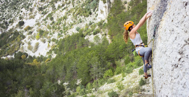 Rock climber ascending cliff Female rock climber ascending rugged cliff. upward mobility stock pictures, royalty-free photos & images