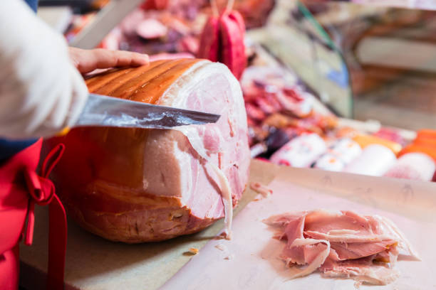 Experienced butcher shop assistant cutting ham to sell it