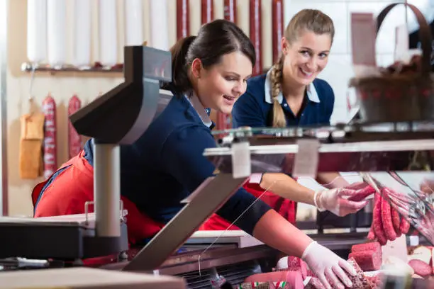 Two sales ladies in butcher shop stuffing the meat display with sausages