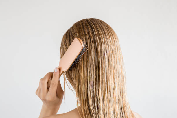 Young woman with comb brushing her wet, blonde, perfect hair after shower on the gray background. Care about beautiful, healthy and clean hair. Beauty salon concept. Back view. Young woman with comb brushing her wet, blonde, perfect hair after shower on the gray background. Care about beautiful, healthy and clean hair. Beauty salon concept. Back view. brushing hair stock pictures, royalty-free photos & images