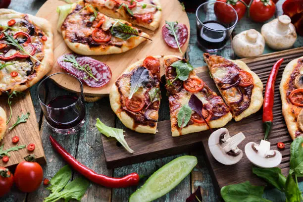 Domestic food. Top view of rustic blue wooden table with homemade pizzas, raw vegetables, mushrooms, salami and red wine above view