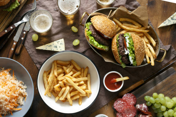 mesa al aire libre con hamburguesa, papas fritas, ensaladas y aperitivos en mesa de madera con cerveza, vista superior. comida al aire libre concepto - dining burger outdoors restaurant fotografías e imágenes de stock